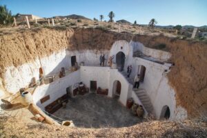 Vue panoramique de Matmata avec ses habitations troglodytiques uniques creusées dans les montagnes, sous un ciel bleu clair. Des escaliers et des ouvertures circulaires se distinguent, illustrant l'harmonie entre ces maisons traditionnelles et le paysage désertique environnant.